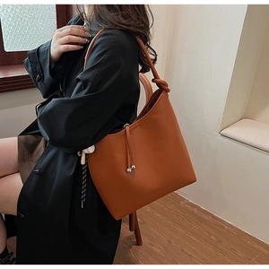 Dettaglio della borsa tote in pelle marrone con coulisse decorativa, perline e tracolla annodata