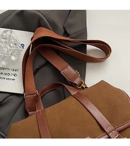 Close-up of brown suede bag with white stitching and wide woven shoulder strap