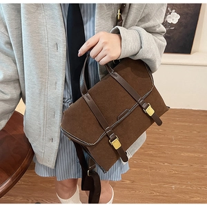 Detail of vintage brown suede satchel featuring double leather straps and gold buckles