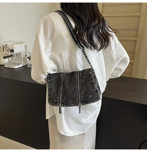 Detail of dark denim crossbody bag featuring dual metal zippers and geometric strap on a model