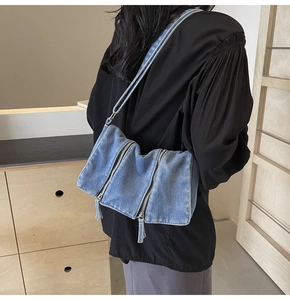 Washed blue denim crossbody bag with decorative silver zippers shown on a model