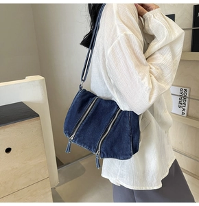 Detail of dark blue denim shoulder bag featuring parallel decorative zippers on front