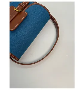 Detail of blue denim saddle bag featuring brown leather trim and contrast stitching