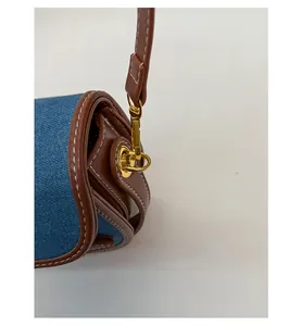 Detail of blue denim and brown leather saddle bag with golden buckle and white stitching