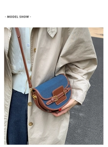 Detail of denim and leather saddle bag with gold metal buckle on a model wearing a trench coat