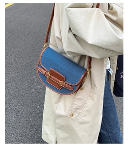 Side view of denim and brown leather saddle bag styled with a beige trench coat
