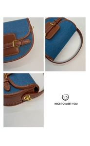 Detail of blue denim saddle bag featuring contrast stitching and golden hardware buckle