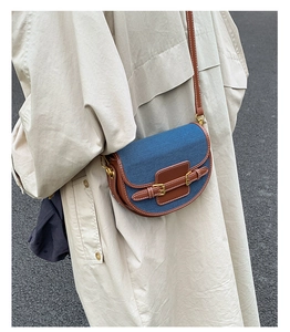 Detail of a color-block saddle bag featuring blue denim and brown leather with gold hardware