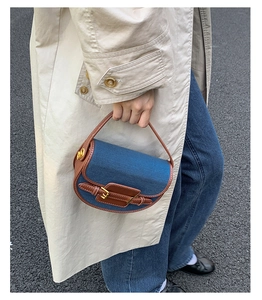 Detail of blue denim and brown leather contrast stitching on a saddle handbag