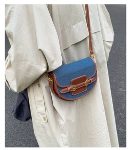 Detail of denim saddle bag with brown leather trim and contrast stitching on trench coat