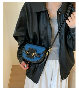 Close-up of blue denim saddle bag with black leather straps and gold buckle details