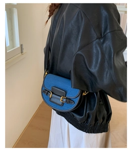Detail of denim saddle bag with gold metal buckles and black faux leather trim