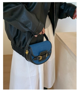 Detail of color-block saddle bag with denim fabric and black leather buckle strap