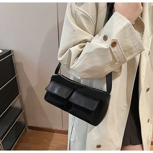 Close-up of black crossbody bag with functional front pockets on beige trench coat