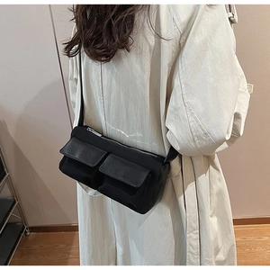 Detail of black suede baguette bag with double front pockets shown on trench coat