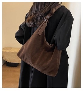 Detail view of large brown suede hobo bag with leather tag on model with black coat