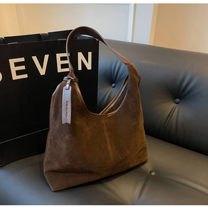 Detailed view of dark brown suede shoulder bag with vertical stitching on leather sofa