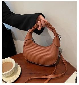 Detail of caramel brown crescent bag with vertical pleats and soft cloud handle on table