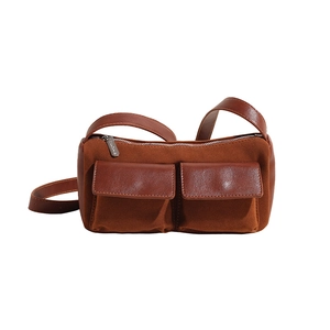 Detail of suede baguette bag featuring brown leather pockets and a metal zipper closure