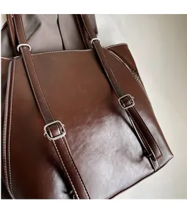 Detail of adjustable long shoulder straps and white contrast stitching on brown tote bag