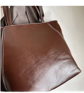 Detailed view of deep brown leather tote with contrasting white stitching and texture