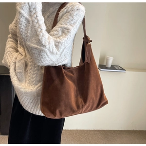 Detail of dark brown suede tote bag with leather tag worn by model in knit sweater