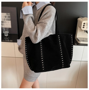 Grand sac cabas en daim noir avec clous argentés porté par un mannequin en intérieur