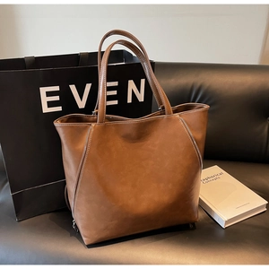 Close-up of brown tote bag with decorative metal zippers and contrast stitching