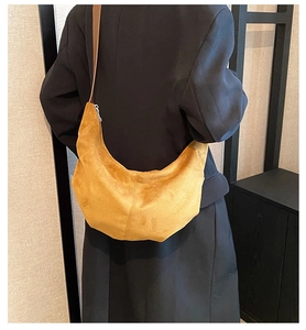 Sac hobo en daim jaune moutarde avec bandoulière porté sur un blazer noir