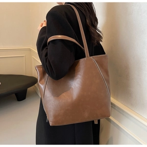 Brown leather tote bag featuring contrast stitching and side zipper details on a model