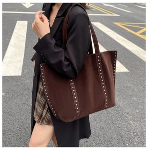 Gros plan sur un sac cabas en daim marron foncé avec rivets argentés au style rétro urbain