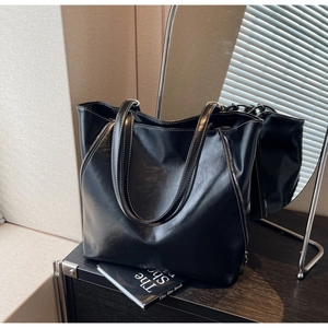 Close-up of black PU leather tote bag featuring contrast white stitching and side zipper details