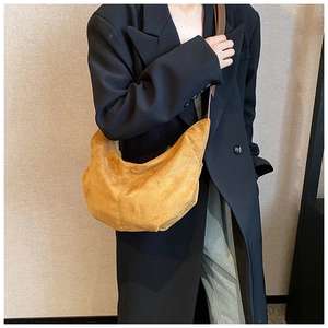 Détail d'un sac demi-lune jaune moutarde en faux daim porté sur un blazer noir chic