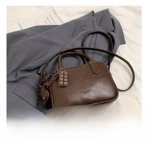 Detail of dark brown leather boston bag featuring a fashion logo and cute charms