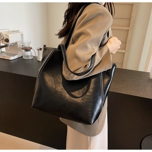 Close-up of black leather tote bag featuring silver zipper details and white stitching