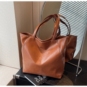 Detail of caramel leather tote bag featuring white stitching and decorative zippers