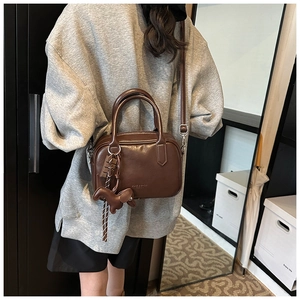 Detail of dark brown leather Boston bag with dog charm and shoulder strap on model