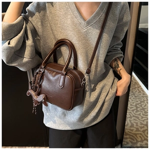 Detail of coffee brown textured leather boston bag with a cute leather puppy charm
