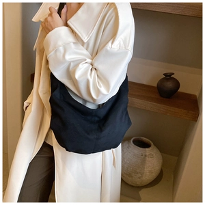Détail d'un sac hobo noir en daim synthétique porté avec un trench-coat beige élégant