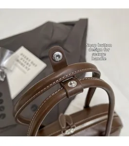 Close-up of brown leather bag showing snap button handle and white contrast stitching