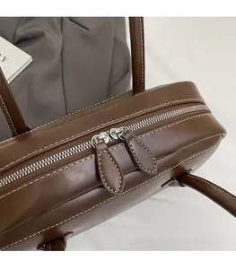 Close-up of smooth double silver zippers and white contrast stitching on brown leather bag