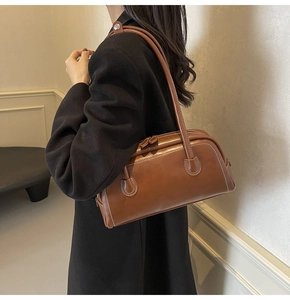 Close-up of brown leather Boston bag with white stitching detail and shoulder strap