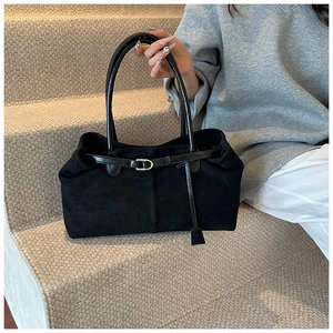 Detail of black suede tote bag with silver buckle and tassel on grey stairs
