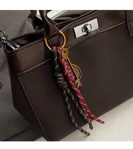 Detail of premium brown leather handbag with woven rope pendant and metal hardware