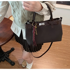 Detail of a dark brown tote bag featuring a silver twist lock and woven charm accessory
