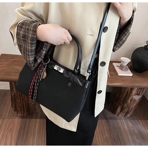 Detail of black trapezoid commuter bag with silver turn-lock and plaid scarf accessory