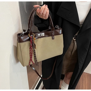 Detail of color-block tote bag with silver turn-lock clasp and woven charm accessory