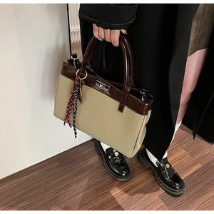 Detail of color-block tote bag with metallic twist lock and woven tassel charm