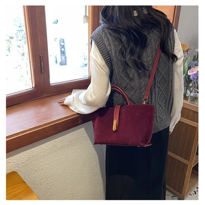 Macro view of matte burgundy suede shoulder bag with elegant gold metal buckle detail