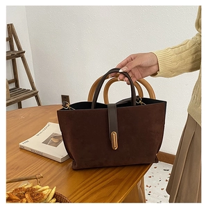 Close-up of a dark brown suede bucket bag with gold hardware on a wooden table